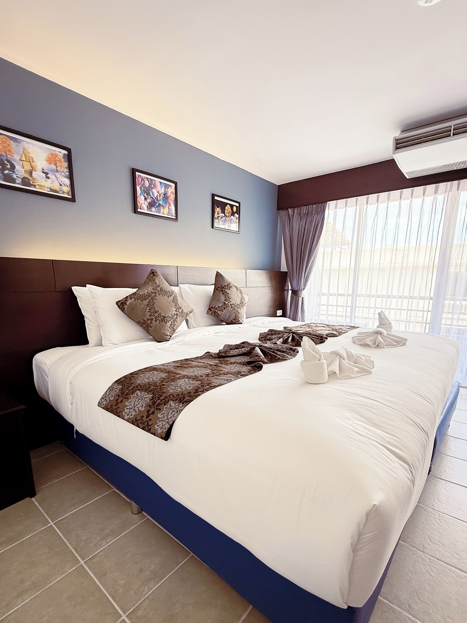 Habitación de hotel con una cama grande, un cabecero, una mesita de noche y una ventana con cortinas.