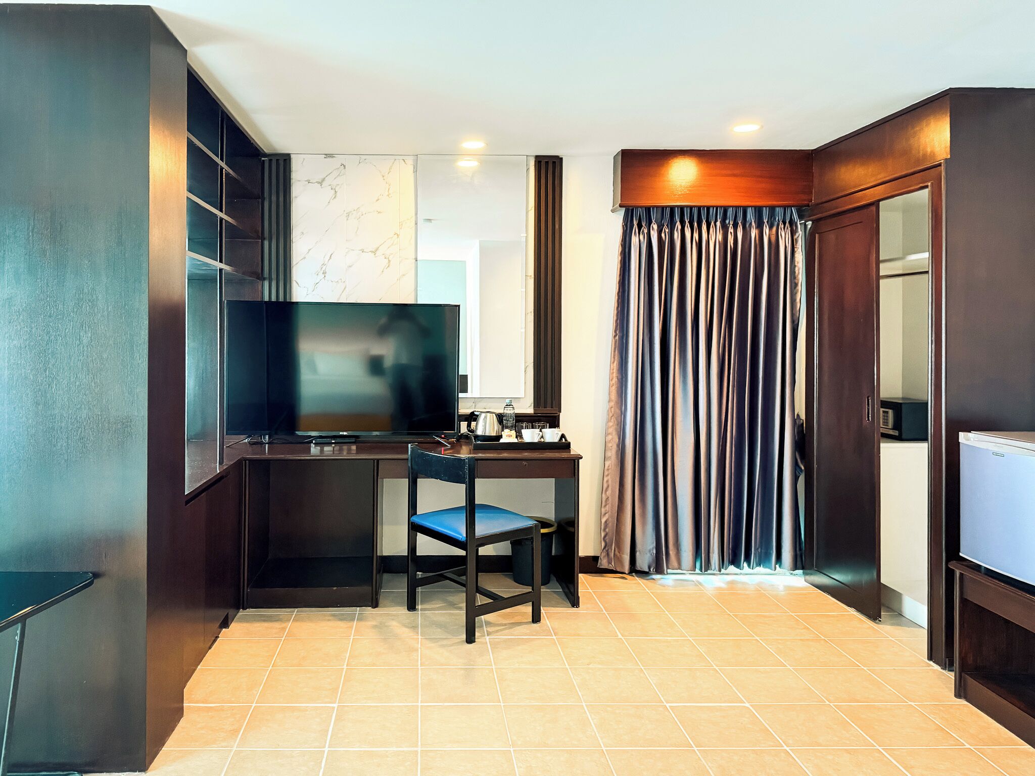 Ein kleines Hotelzimmer mit Fernseher, Schreibtisch, Stuhl, Kleiderschrank und Vorhang.