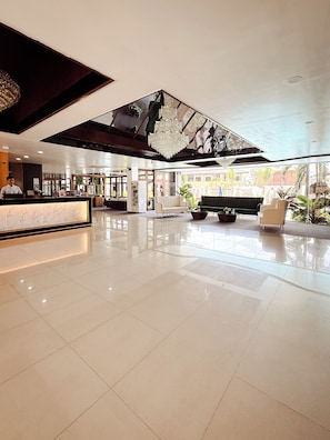 Un vestíbulo espacioso con un mostrador de recepción de mármol, un gran candelabro y una zona de estar con sofás y sillones.