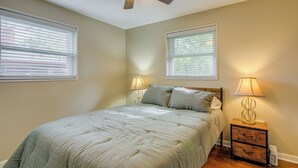 Une chambre à coucher comprenant un lit, deux lampes de chevet, un ventilateur de plafond et deux fenêtres équipées de stores.