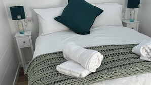 A neatly made bed with a green knitted blanket, white pillows, and rolled towels. There are two bedside tables with lamps and a framed artwork on the wall. - A secluded and tranquil cabin ideal for exploring Lewis and Harris (Isle of Lewis)