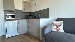 A modern kitchen with a microwave, refrigerator, and cabinets. There's a gray sofa with a floral pillow and a small white table. - A secluded and tranquil cabin ideal for exploring Lewis and Harris (Isle of Lewis)