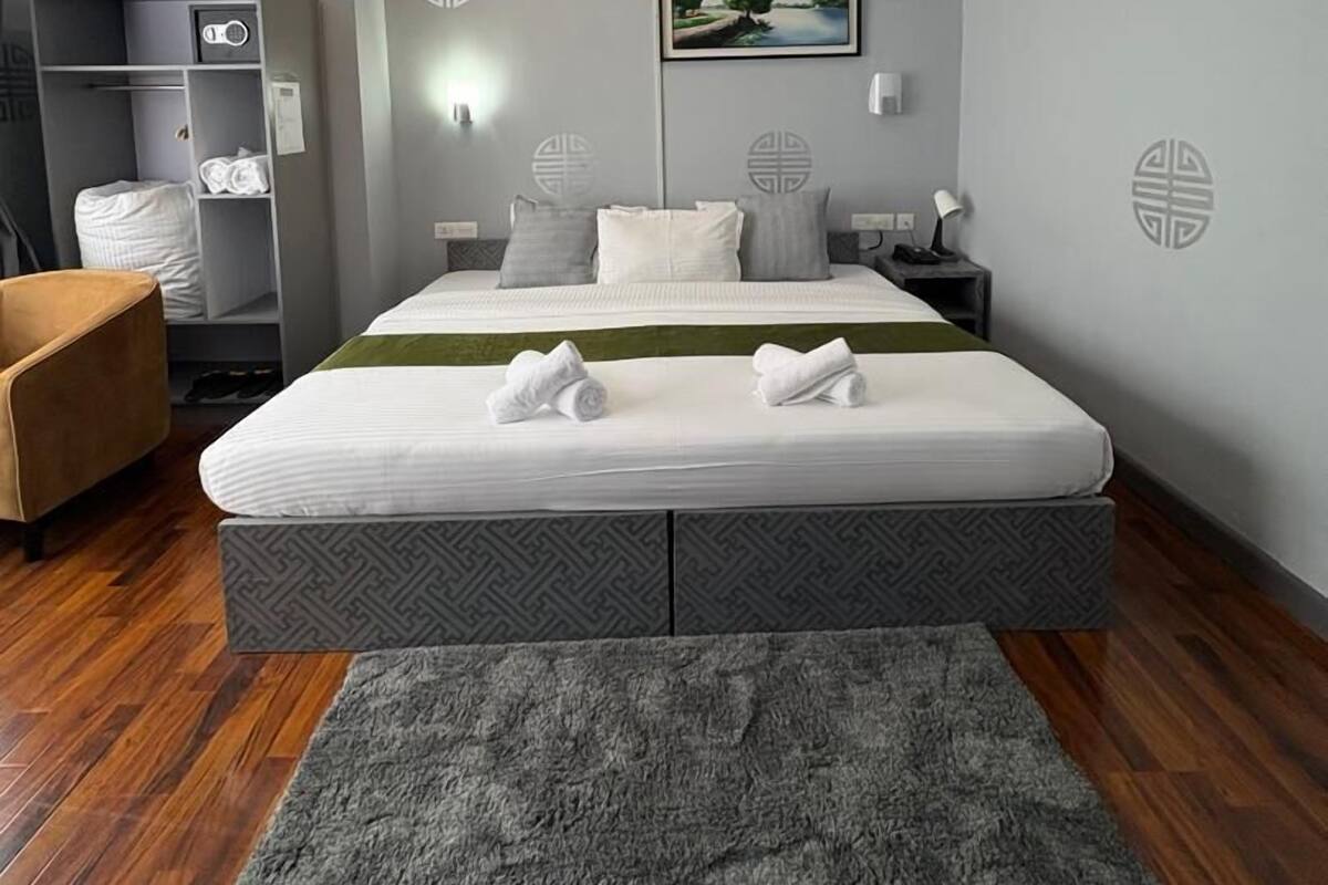 A modern hotel room with a large bed, a wardrobe, a desk, and a chair.