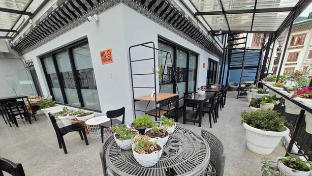 An outdoor seating area with tables and chairs, surrounded by potted plants, under a covered patio. - The Gochuka Hotel (Thimphu)