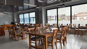A spacious dining area with wooden tables and chairs, large windows with a view of the street, and a modern ceiling design. - The Gochuka Hotel (Thimphu)