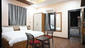 A hotel room with a bed, two chairs, a wardrobe, a mirror, and an air conditioning unit.
