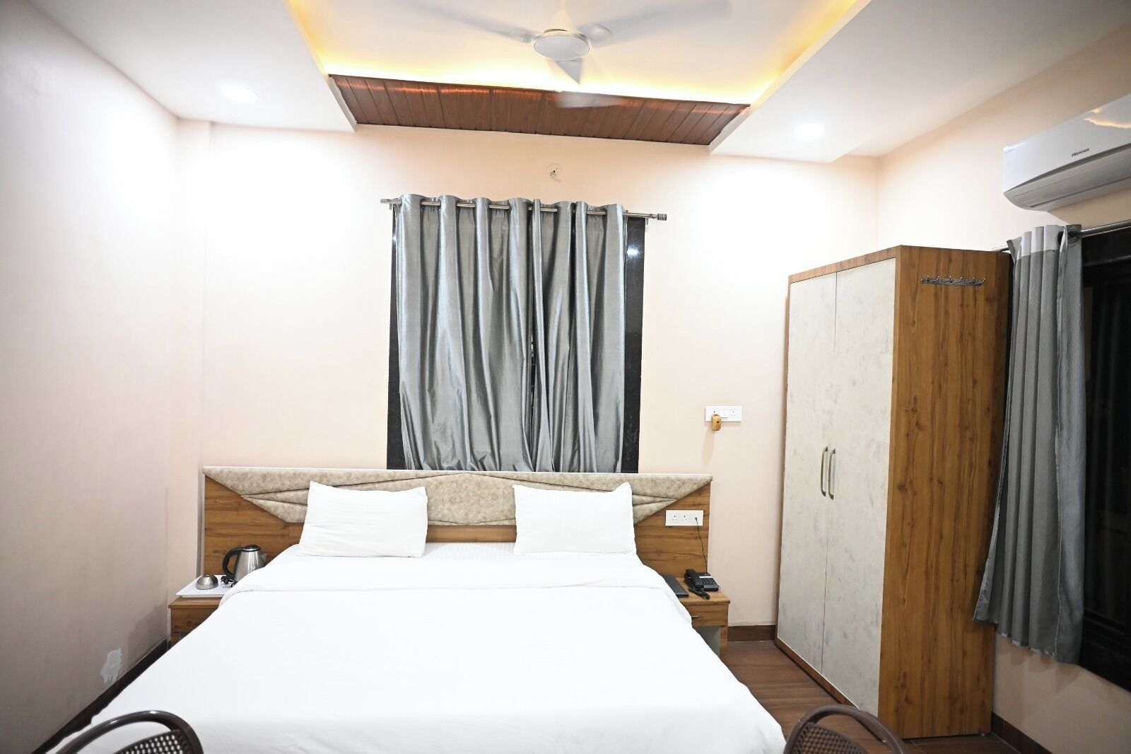 A hotel room with a bed, a wardrobe, a desk with a telephone, and a ceiling fan.