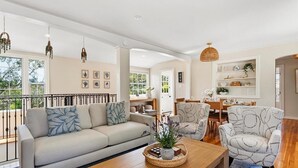 Ein modernes Wohnzimmer mit einer Couch, Sesseln, einem Couchtisch und einem Essbereich mit Stühlen und Tisch.