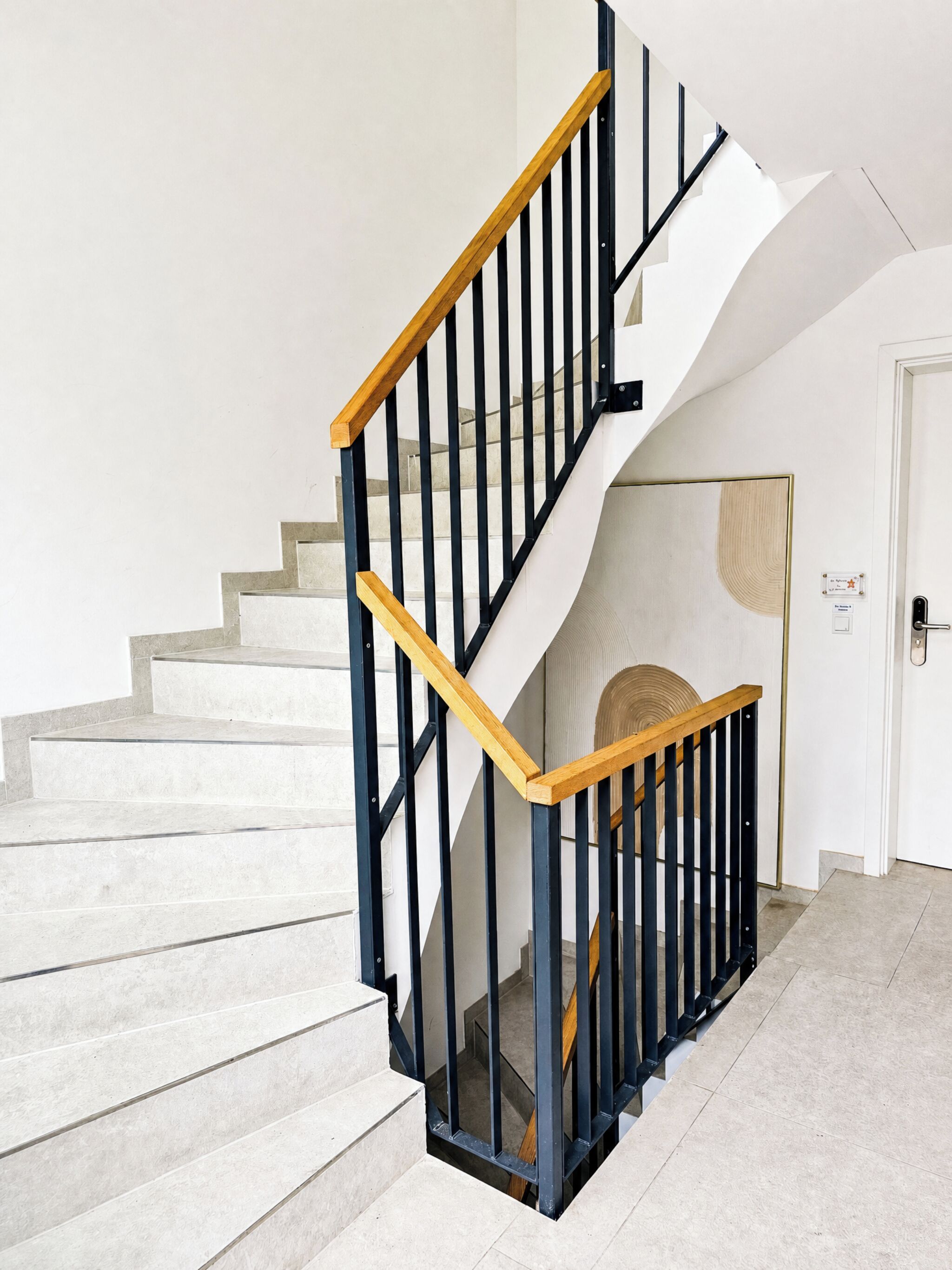 A staircase with a wooden handrail and black balusters, leading to a landing with a white door.