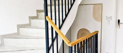 A staircase with a wooden handrail and black balusters, leading to a landing with a white door.