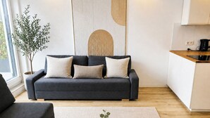 Una sala de estar moderna con un sofá, una mesa de centro con una planta, y una zona de cocina con una tetera.