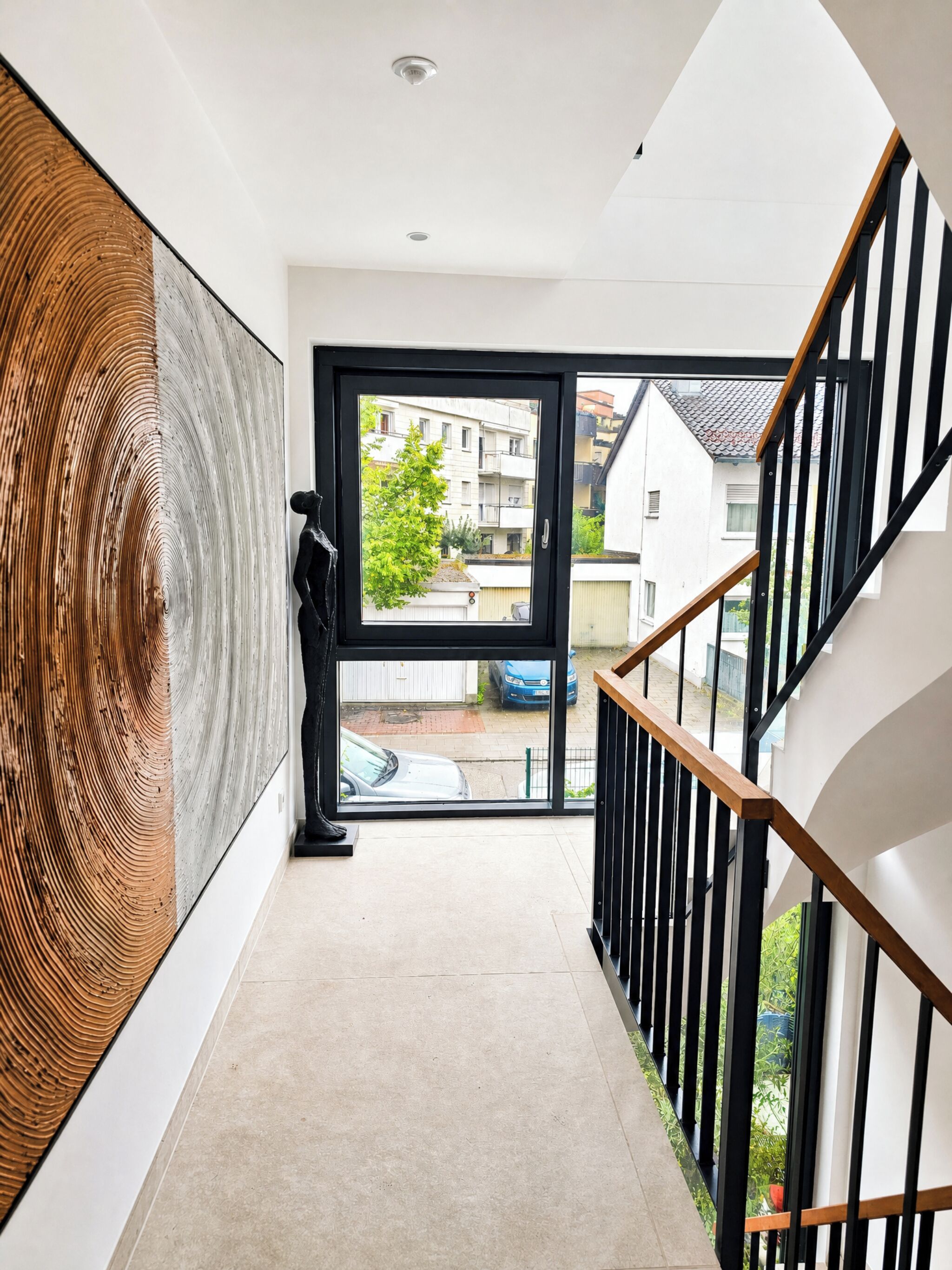 A modern interior with a staircase, a large abstract artwork, and a view of the outside.