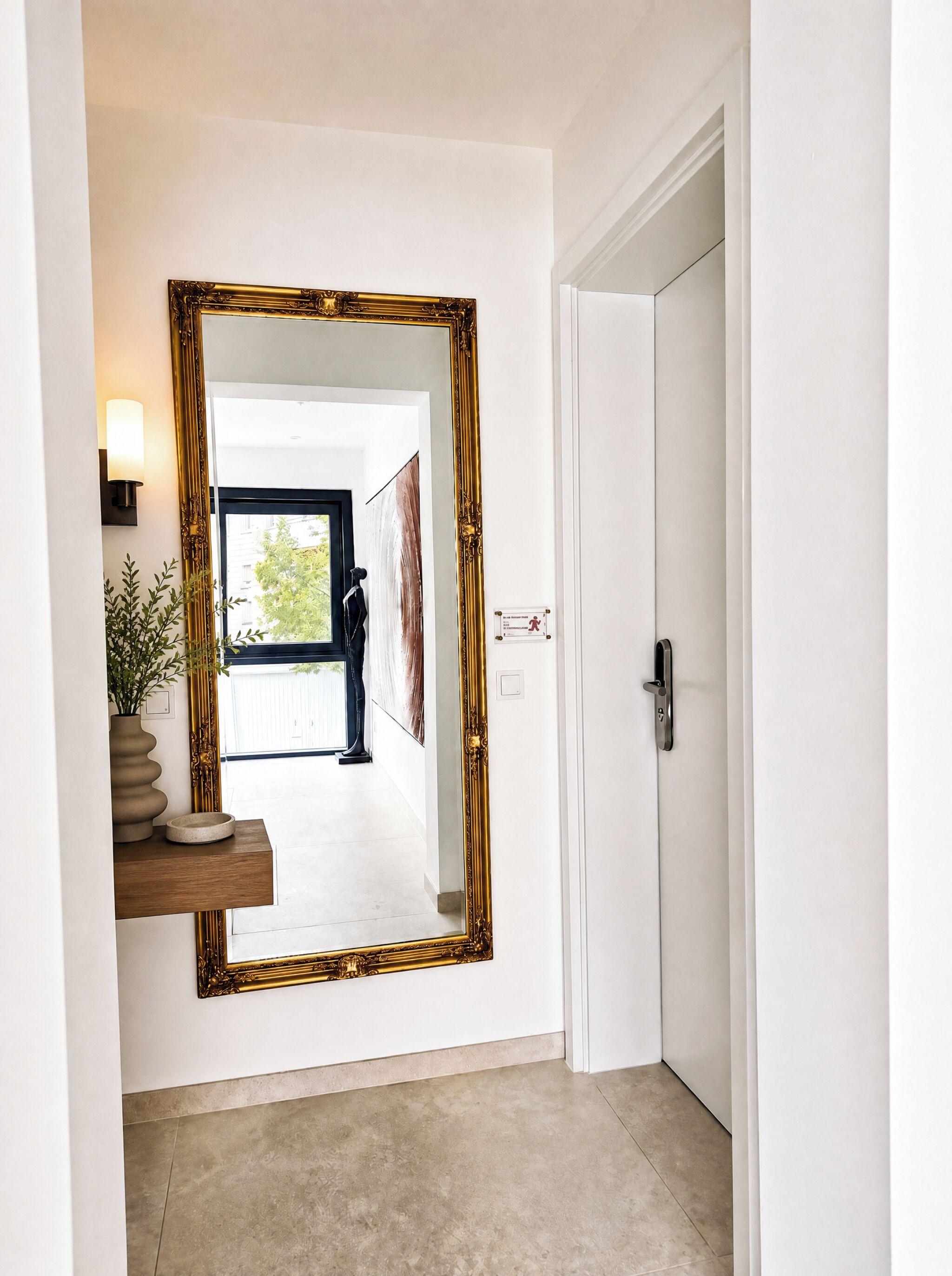 A hallway with a large ornate mirror, a potted plant, and a door.