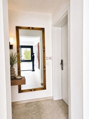 A hallway with a large ornate mirror, a potted plant, and a door. - L Beautiful newly built apartment -9 min to Octoberfest (München)