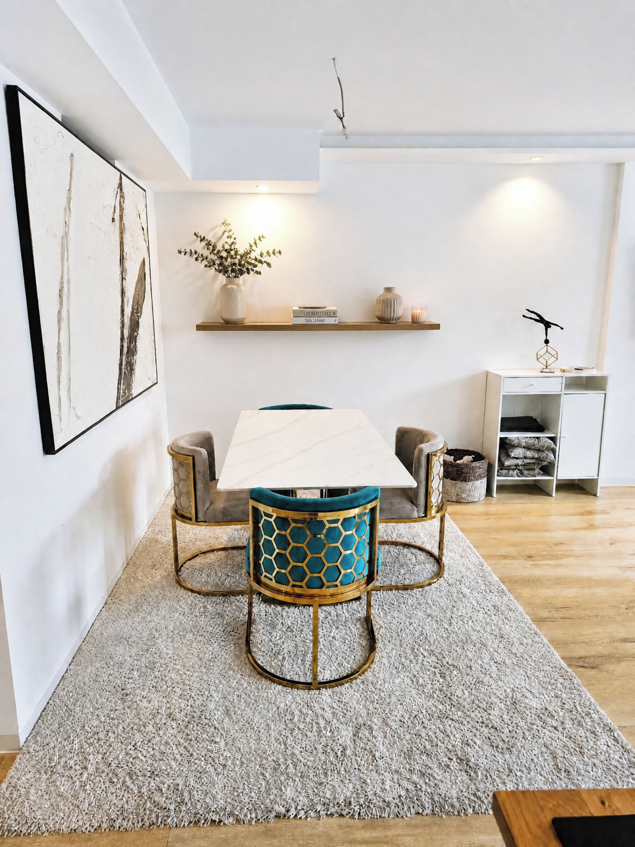 A modern dining area with a white table, two chairs with blue cushions, and a decorative vase on a shelf.