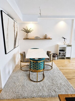 A modern dining area with a white table, two chairs with blue cushions, and a decorative vase on a shelf. - L Beautiful newly built apartment -9 min to Octoberfest (München)