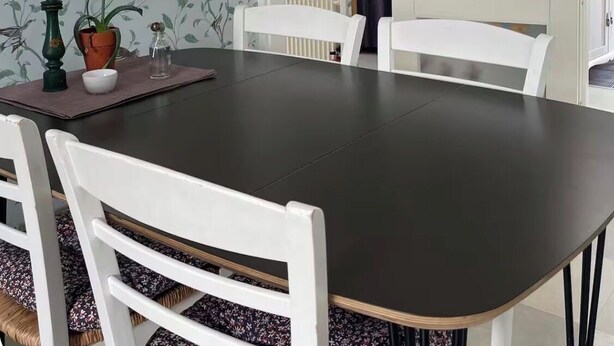 Ein Essbereich mit dunklem Tisch, weißen Stühlen, einer Hängeleuchte und blumengemusterten Tapeten.