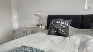 Ein Schlafzimmer mit einem Bett, Kissen, einem Nachttisch mit Lampe und einem an der Wand befestigten Regal.