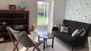 Ein Wohnzimmer mit einem schwarzen Sofa, einem Holzregal, einem Klappstuhl und einem kleinen Tisch.