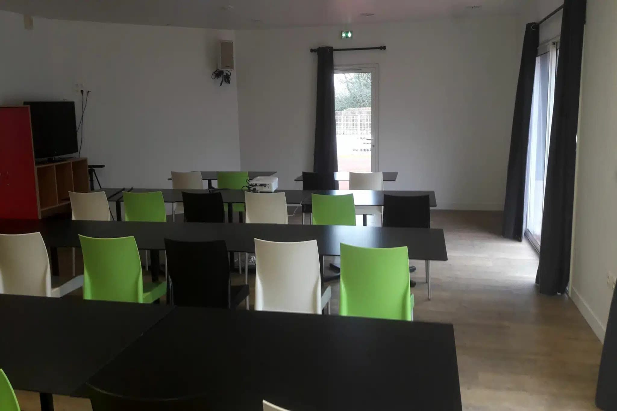 Ein Konferenzraum mit Tischen, Stühlen, einem Fernseher und einem fenster mit Vorhängen.