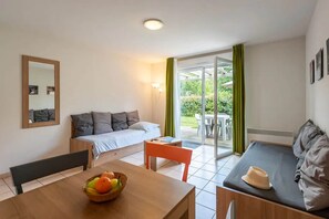 Ein Zimmer mit einem Bett, einem Sofa, einem Esstisch mit Obstschale und einer Glastür zum Außenbereich.