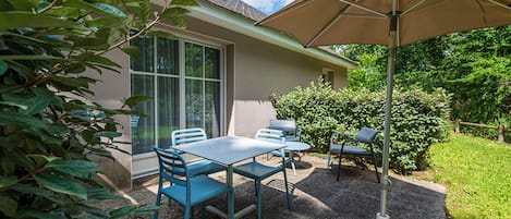A patio with a table and chairs, a large umbrella, and a house with a window and door.