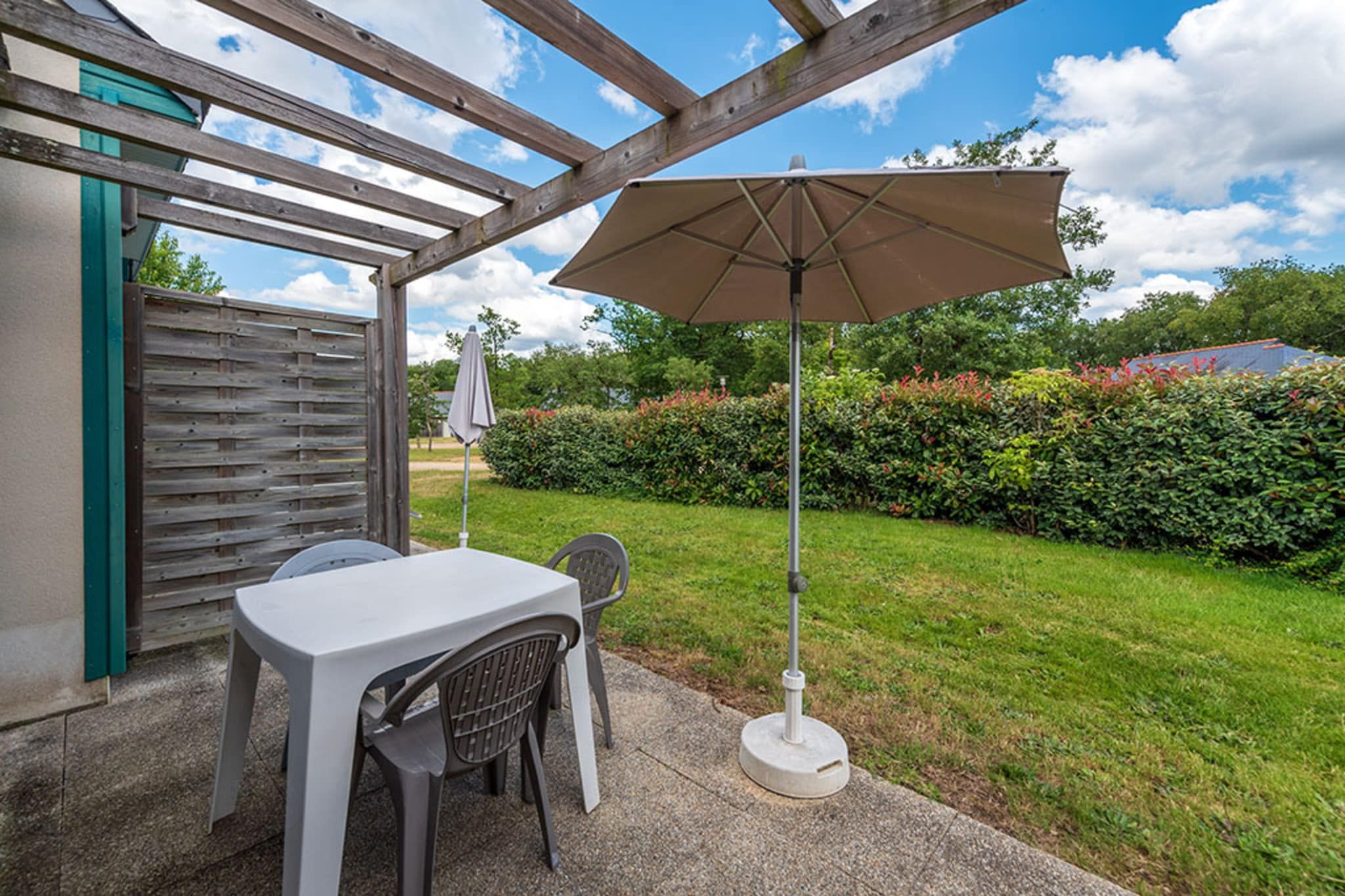 An outdoor patio with a table and chairs, a wooden pergola, and a large umbrella.