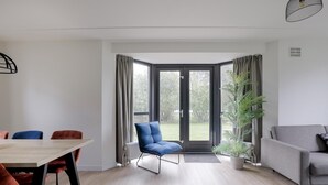 Een moderne woonkamer met een eethoek, een blauwe stoel, een grijze bank en een groot raam met gordijnen.