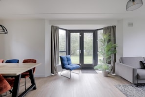 A modern living room with a dining area, a blue chair, a grey sofa, and a large window with curtains. - Lakeside Retreat with Garden for 6 (Ewijk)