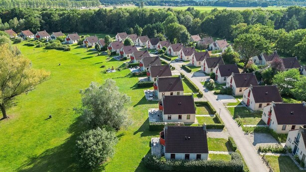 Een woonwijk met rijwoningen, omgeven door groene velden en bomen.