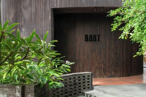 Una puerta de madera con el texto 'BAAT' y una jardinera de ladrillo con follaje verde.