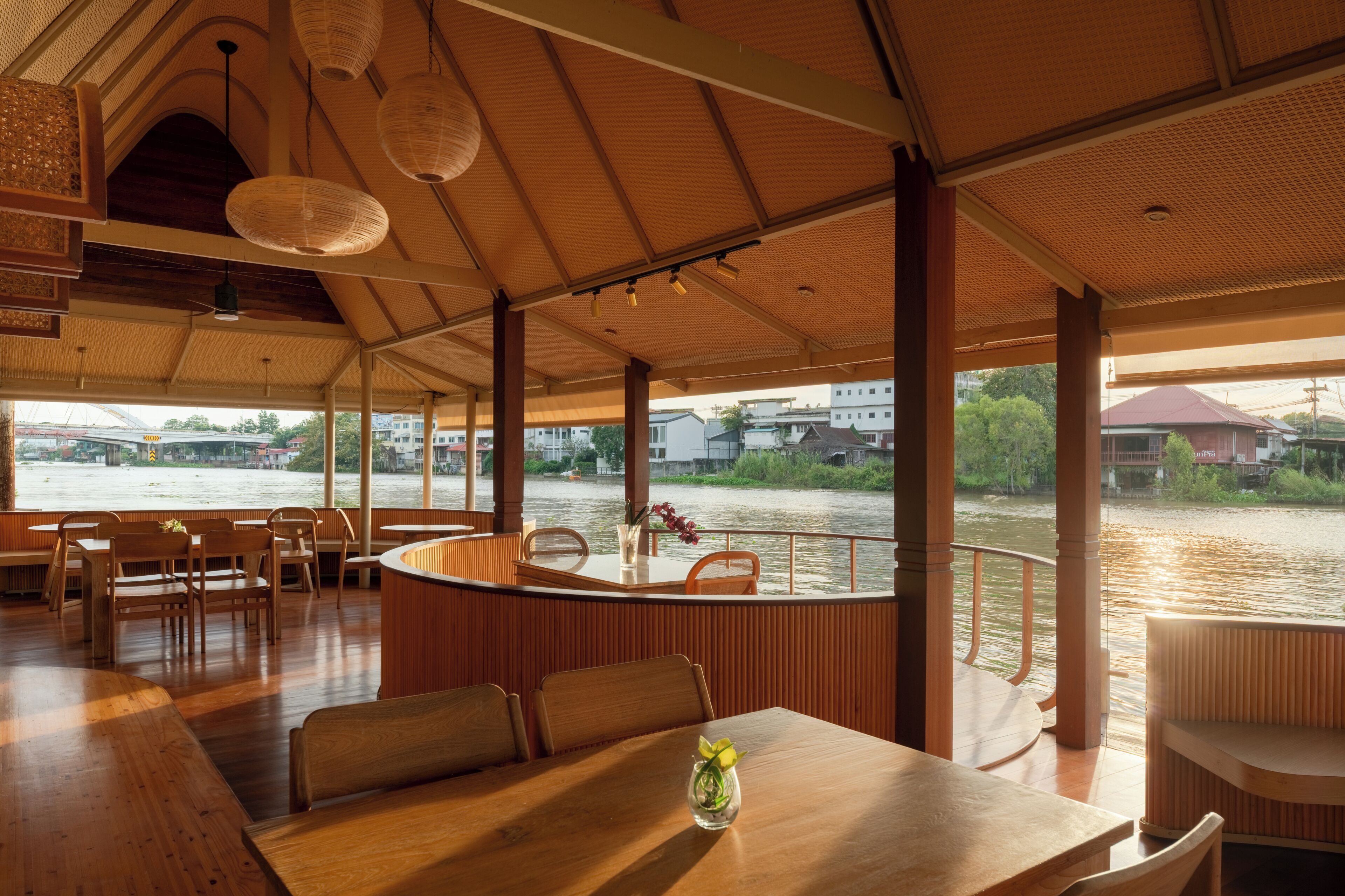 Un restaurante con mobiliario de madera, vistas a un río y una zona de estar al aire libre cubierta.