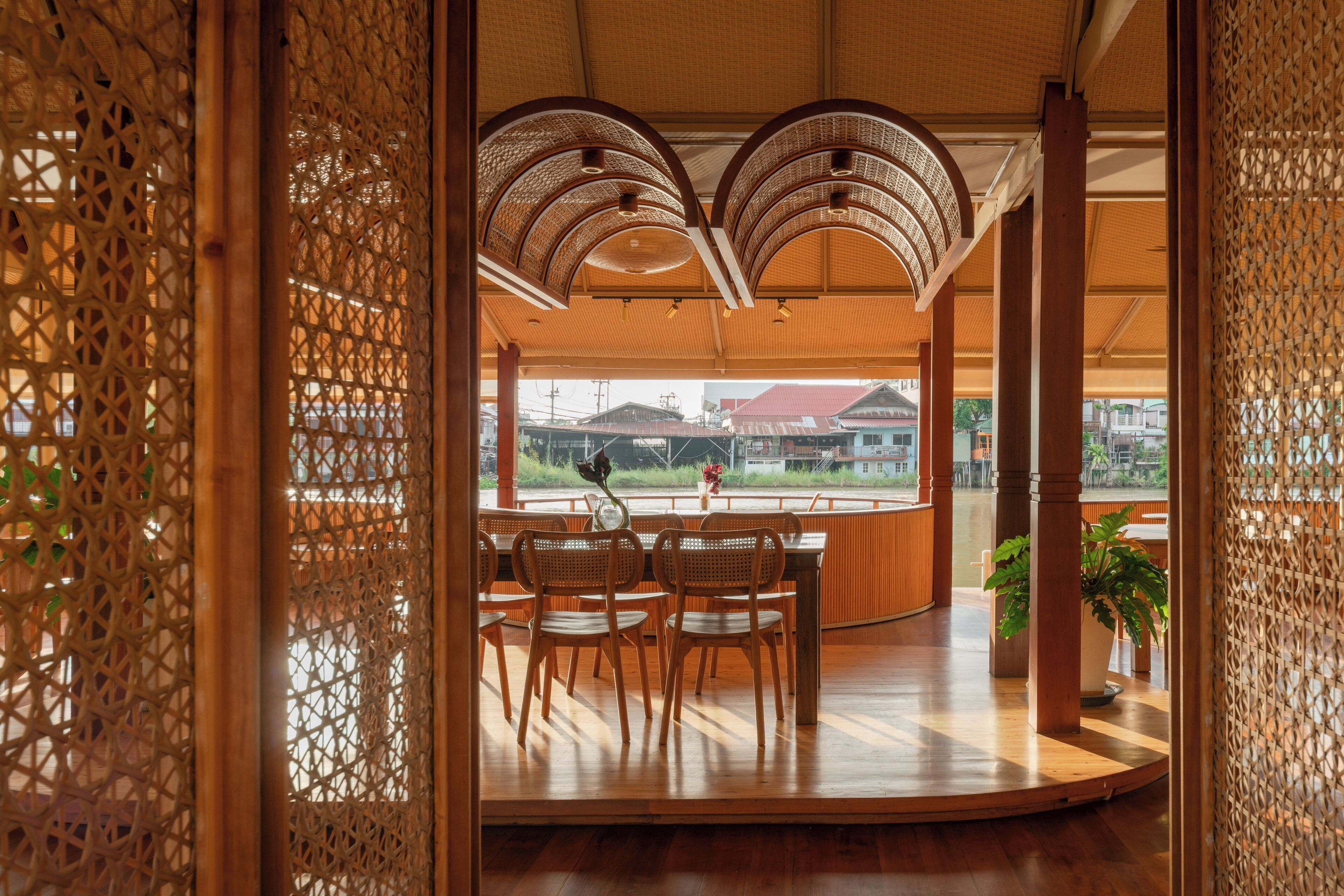 An interior with a wooden table and chairs, a view of the outside, and a ceiling with a woven pattern.