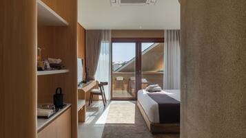 A hotel room with a bed, a desk, a chair, a small kitchenette, and a sliding glass door leading to a balcony.