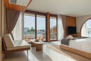 Habitación de hotel con cama, televisor, zona de estar con mesa y amplios ventanales con vistas a la ciudad.