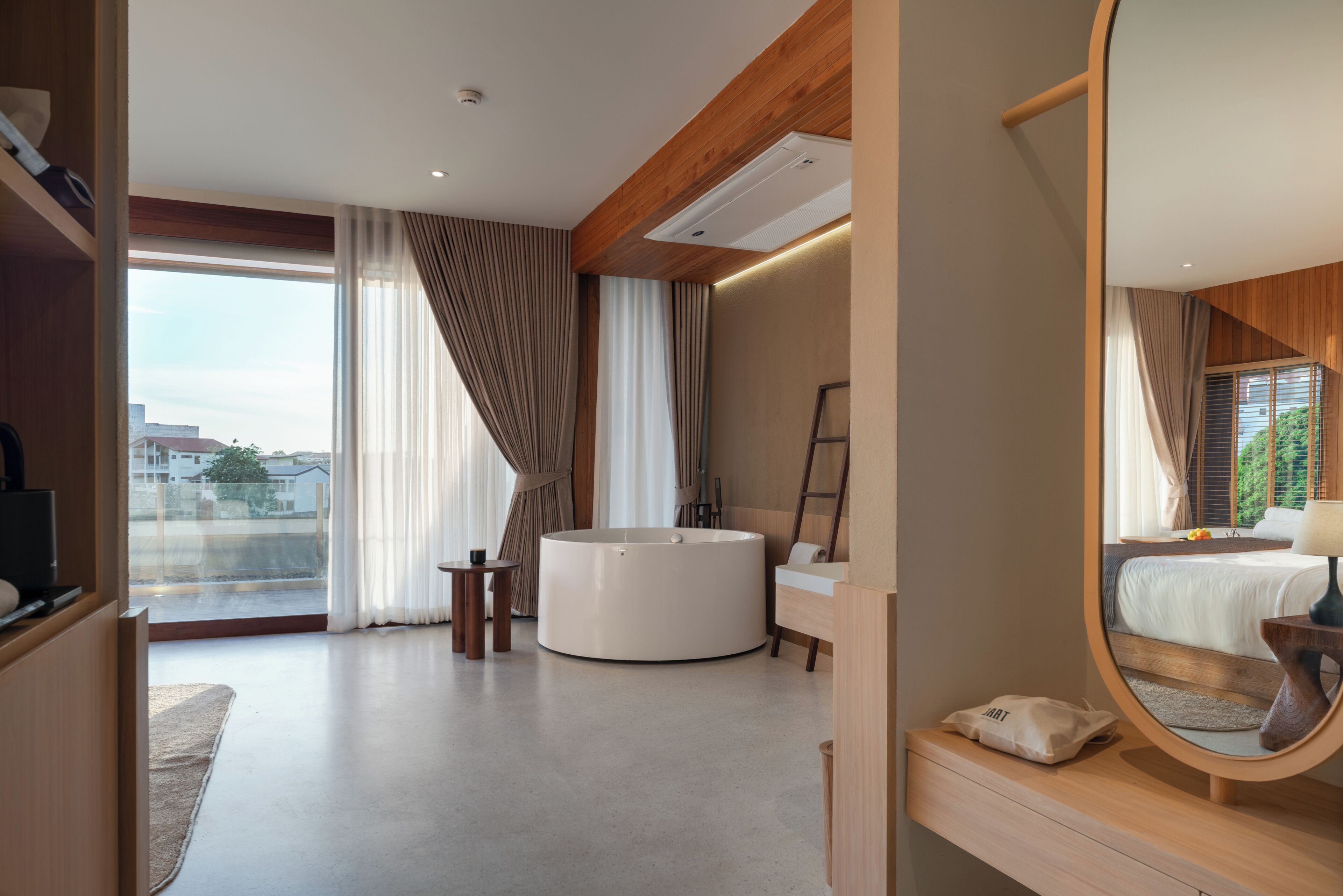 Una habitación de hotel moderna con una cama grande, una bañera redonda, un tocador con espejo y vistas de la ciudad a través de amplias ventanas.