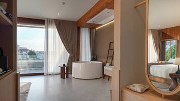 Una habitación de hotel moderna con una cama grande, una bañera redonda, un tocador con espejo y vistas de la ciudad a través de amplias ventanas.