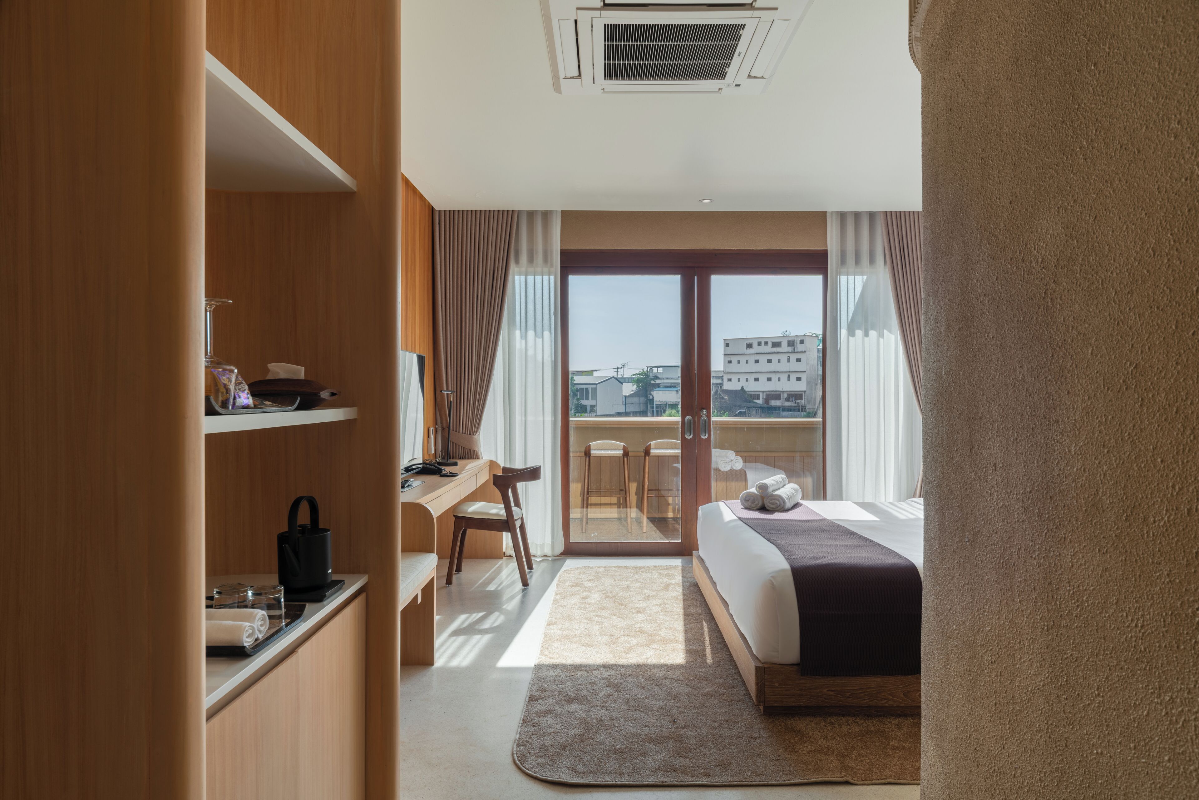 Habitación de hotel con cama, escritorio, silla, armario y vistas al exterior.