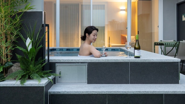 Iemand ontspant in een jacuzzi met een fles wijn en een glas op de rand.