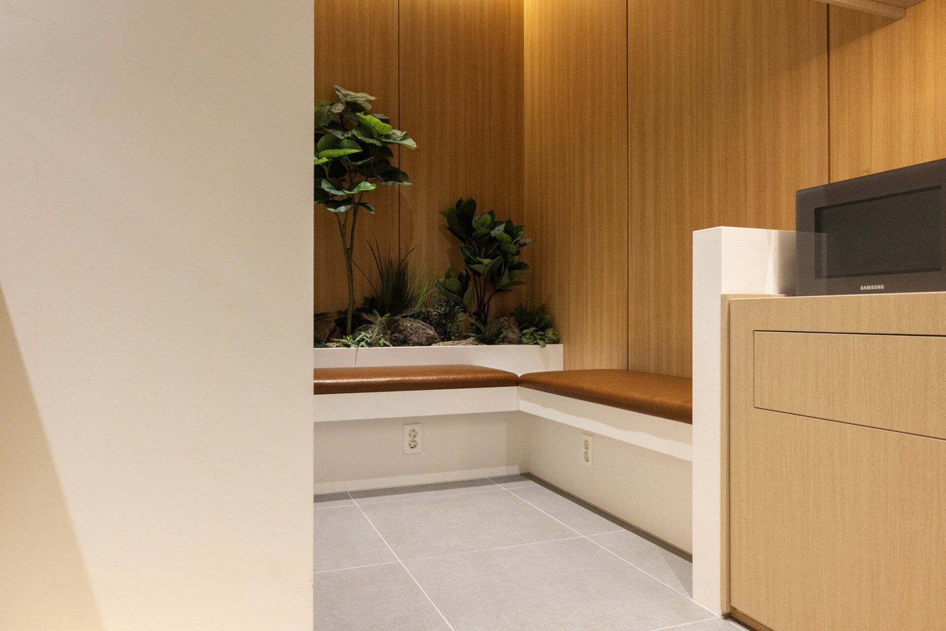 Esquina de una habitación con un armario de madera, un banco y un pequeño arreglo de plantas.