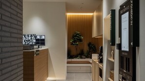 Een receptie met een receptiebalie, een monitor waarop beelden te zien zijn, een plant en een kiosk voor zelfservice-inchecken.
