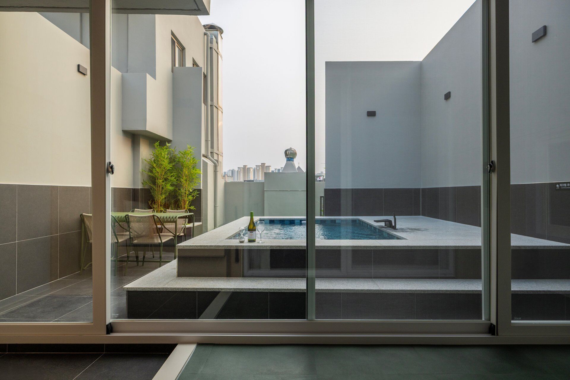A rooftop pool with a glass enclosure, a table with chairs, and a potted plant.