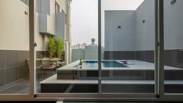 A rooftop pool with a glass enclosure, a table with chairs, and a potted plant.