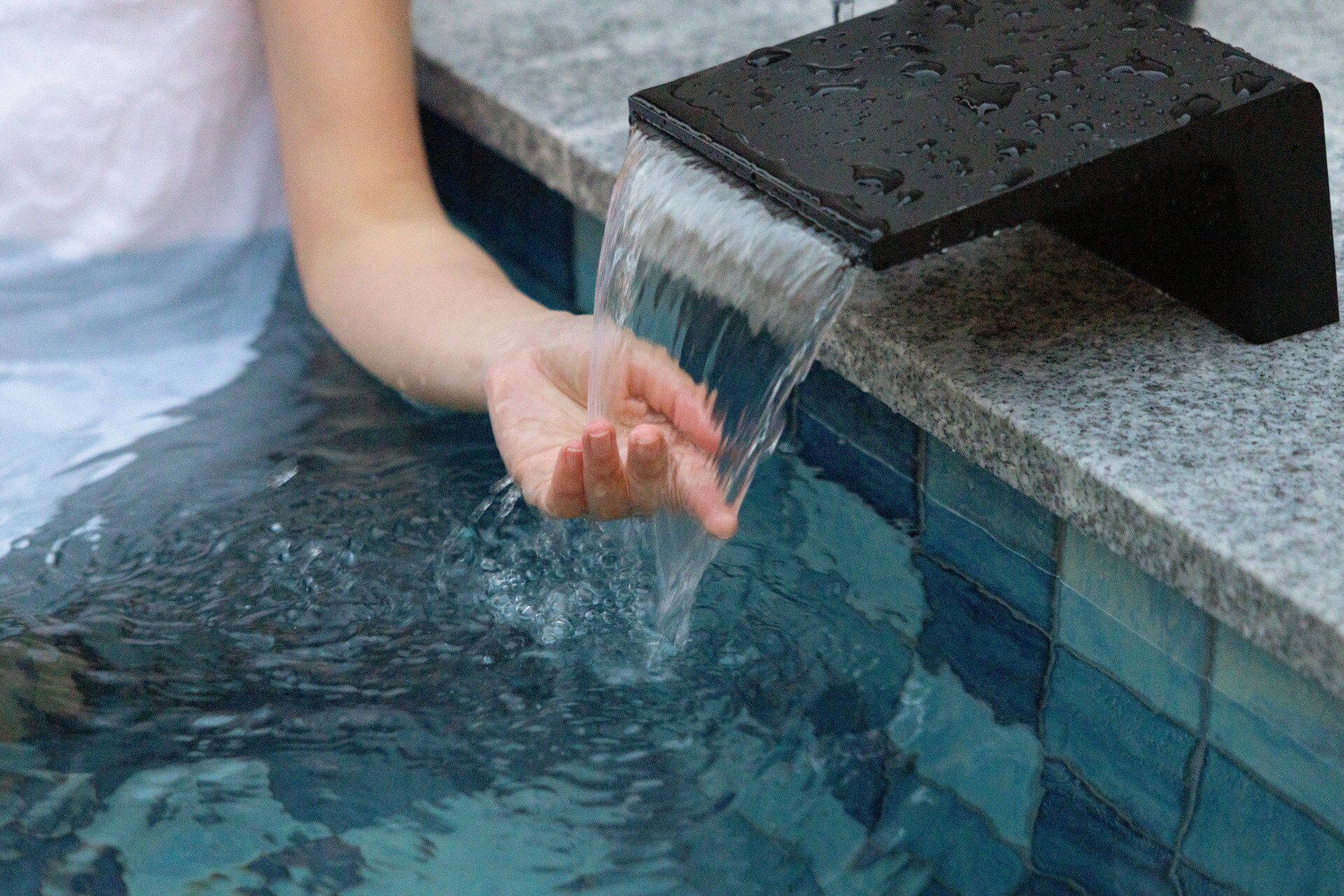 Una mano sumergiéndose en una piscina, con agua saliendo de un grifo.