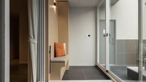 Een moderne badkamer met een douchecabine van glas, een bankje met kussen en een zichtbare lichtschakelaar aan de muur.