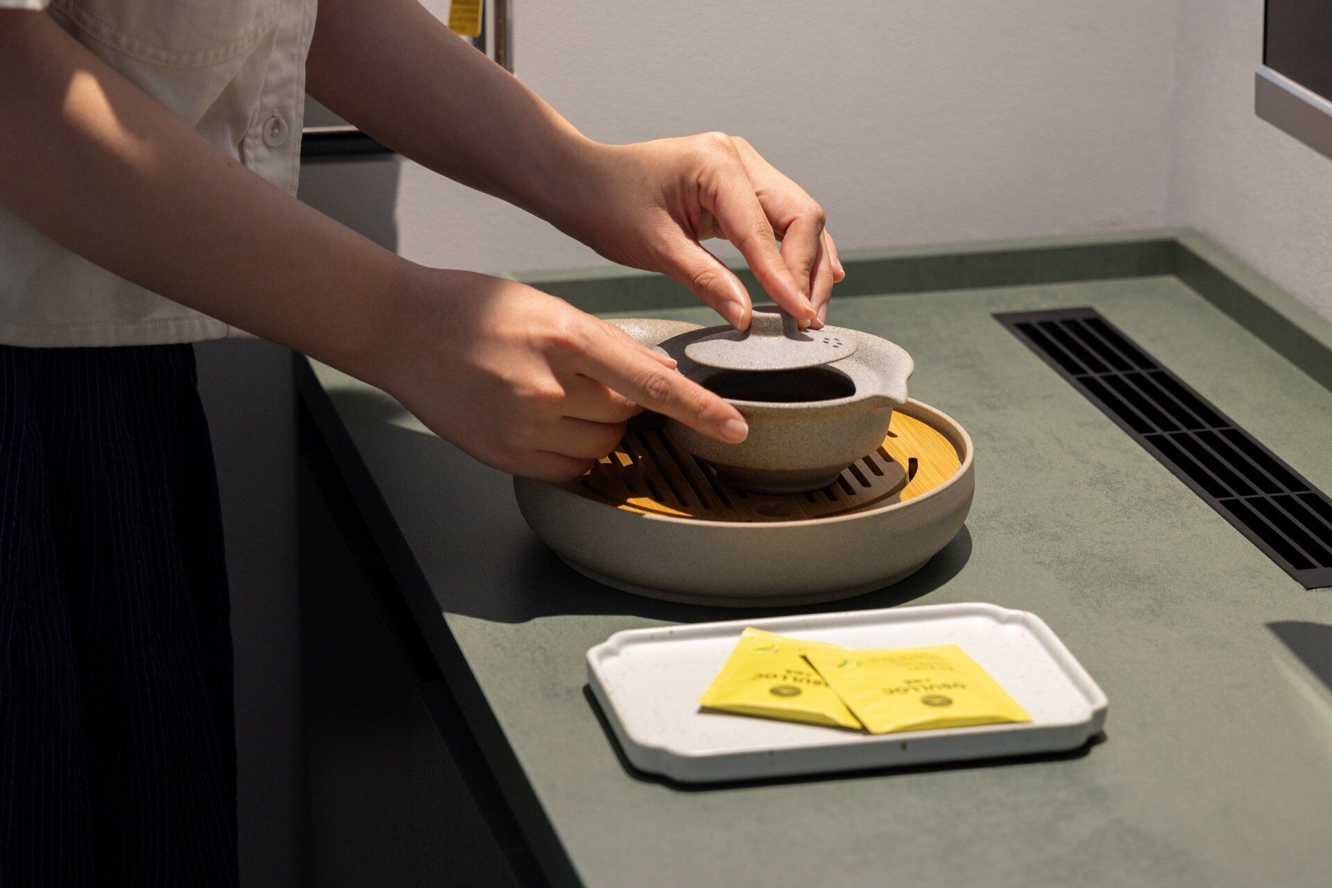 A person placing a lid on a ceramic pot on a tray.
