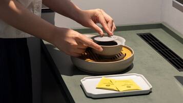 A person placing a lid on a ceramic pot on a tray.