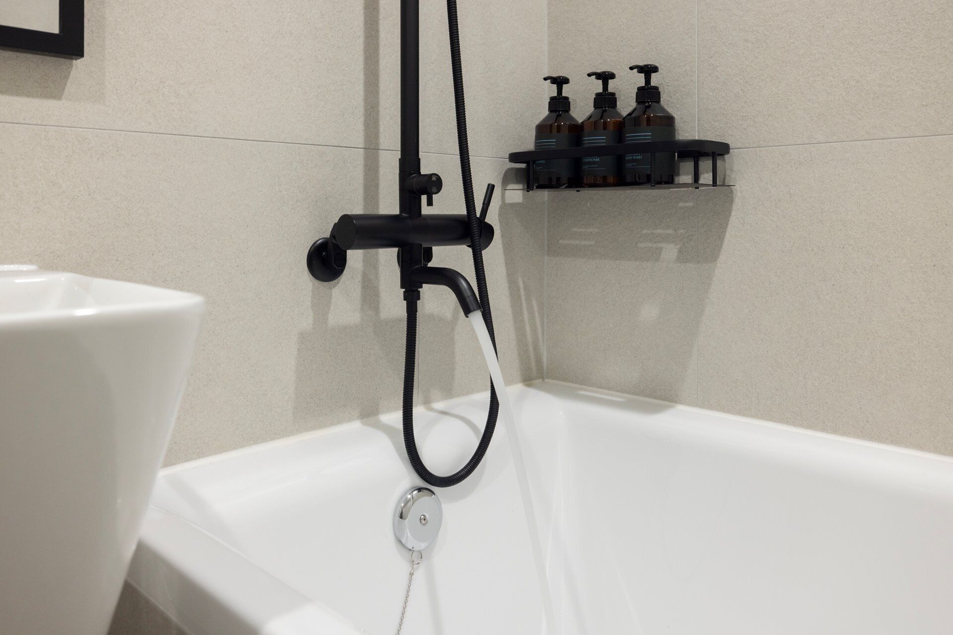 Una bañera con ducha de mano, un lavabo blanco y una estantería con artículos de aseo.