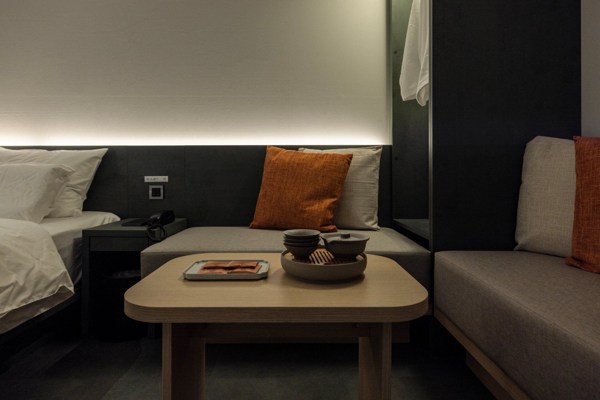 A hotel room with a bed, a sofa, a small table with a bowl and a book, and a wall-mounted phone.