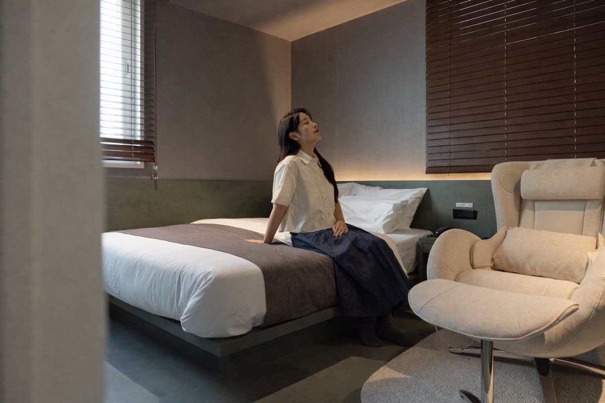 Un dormitorio con cama, una silla y una mesita de noche.